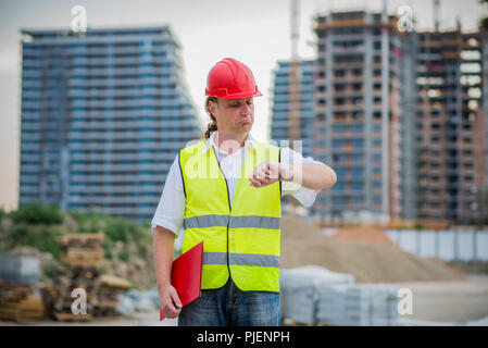 Engineer on a construction site looking at his watch with blurry buildings in the background Stock Photo