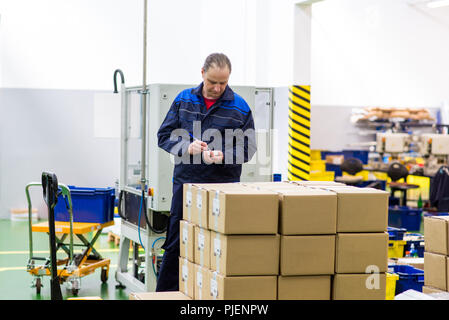 Factory worker taking notes while checking boxes in factory warehouse Stock Photo