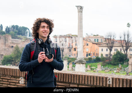 Handsome young tourist with curly hair taking photos of Roman forum in Rome, Italy. Young man travel with his camera Stock Photo