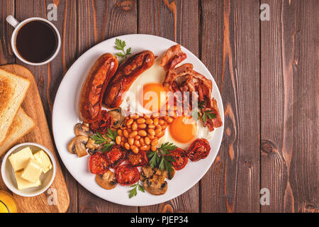 Traditional full English breakfast with fried eggs, sausages, beans, mushrooms, grilled tomatoes and bacon on wooden background. Top view Stock Photo
