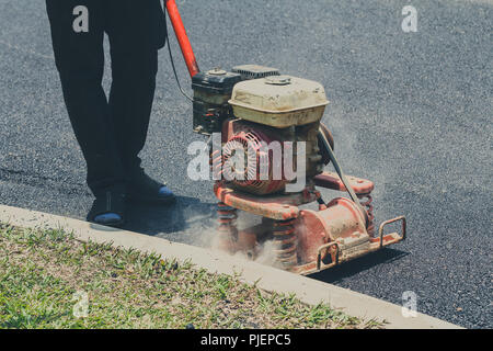 Worker uses vibratory plate compactor compacting asphalt at road repair Stock Photo