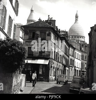 1950s, historical, a view of rue Norvins,a cobblestone street in the Montmartre district of Paris, famous for its artists, showing the decaying building housing the old Parisan cafe, Le Consulat and in the background, the domes of of the Roman Catholic church, Sacre-Coeur. The classic french car, the Citroen 2CV can be seen in the pciture. Stock Photo