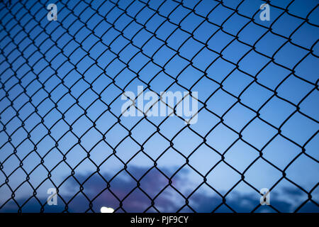 Dark blue sky through wire mesh fence. Blur background, close up view of link cage, wallpaper. Stock Photo