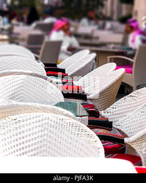 Tables of street cafe  covered with white tablecloth. In the background, a group of men sitting at a table in traditional arabic clothes Stock Photo