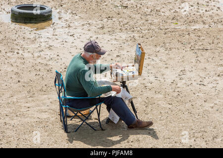 Man with oil painting at easel at low tide on the beach at Margate,Kent, England, Uk. Stock Photo