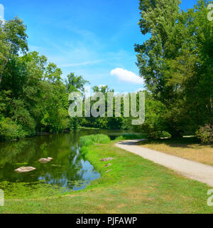 Small picturesque lake in city park and bright blue sky. Stock Photo