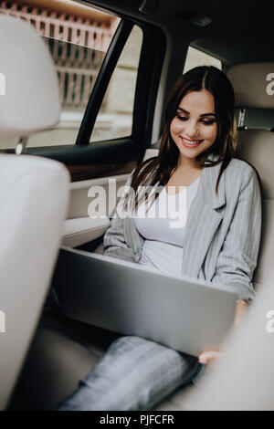 Businesswoman with laptop receiving a phone call on the backseat of a car. Female entrepreneur working during travelling to office in a car. Stock Photo