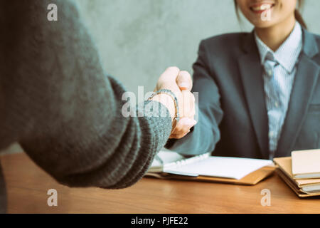 Two Asian businesswomen shaking hands over a desk as they close a deal or partnership, focus to hands of young Asian lady Stock Photo