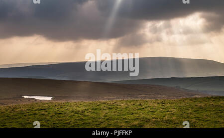 Crepuscular rays of sunlight shine through heavy rain clouds over a moorland countryside landscape in Yorkshire, UK. Stock Photo