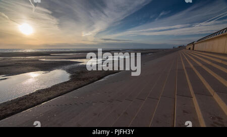 The sun sets over the Irish Sea, lighting up puddles on the sands of Blackpool Beach, seen from the steps of the Promenade sea wall. Stock Photo