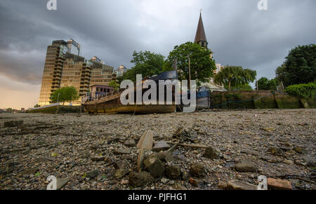 Houseboats are beached on the side of the River Thames at low tide beside Battersea Church in west London. Stock Photo