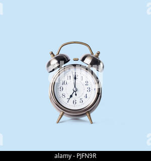 Retro classic alarm clock with bell, twin, showing seven o'clock standing on flat surface Isolated on blue Copy space Stock Photo