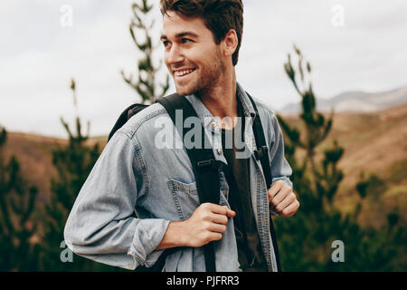 Man walking through a forest wearing a jacket and backpack. Happy man on a holiday hiking in a countryside location. Stock Photo