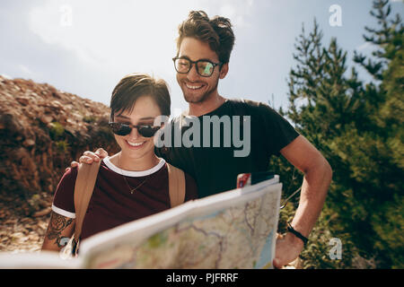 Smiling man and woman standing in forest looking at map. Couple using a map to locate their destination. Stock Photo