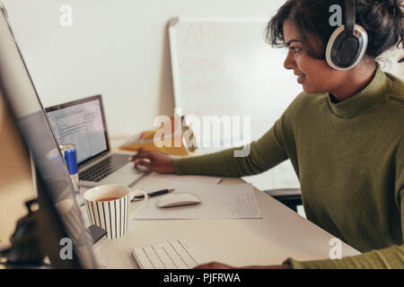Female programmer working in office. Woman looking at laptop while coding on desktop computer. Stock Photo