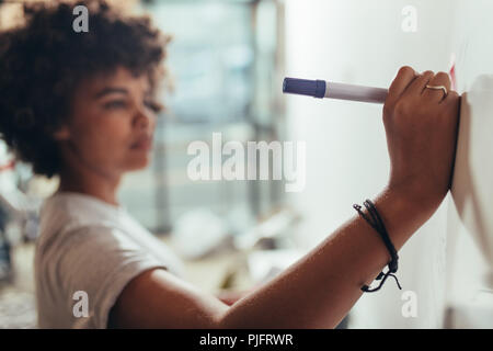 Close up of woman writing on white board during a business project meeting. Focus on female hands writing with a marker pen on presentation board. Stock Photo