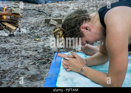 Close up picture of a young hippie woman practicing yoga with multiple silver bracelets and rings in a fire camp Stock Photo