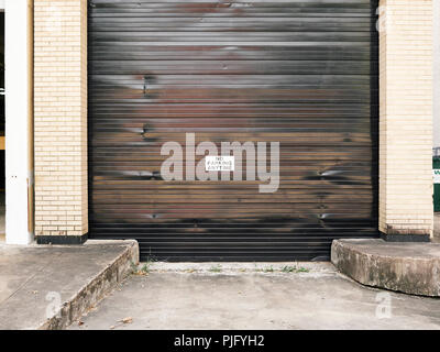 No parking any time warning sign posted on large receiving roll top garage door on city street in Montgomery Alabama, USA. Stock Photo