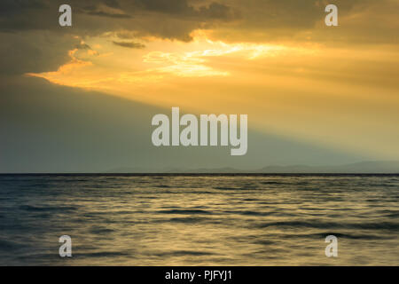 Amazing golden sun-rays passing through the large hole in dramatic clouds over the sea Stock Photo