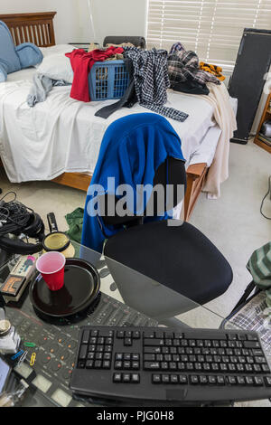 Messy, cluttered teenage boys bedroom with piles of clothes.  Vertical view. Stock Photo