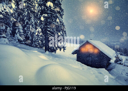 Christmas snowfall in mountains. Beautiful winter christmas night on hills. Winter landscape with wooden house and christmas forest. Xmas background. Stock Photo