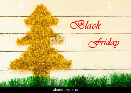 Golden Christmas decoration in the form of trees, green tinsel in the form of grass and inscription Black Friday, in red letters on white wooden board Stock Photo