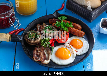 Close view English Breakfast in a pan with fried eggs, sausages, bacon, mushrooms, jam and orange juice on wooden background Stock Photo