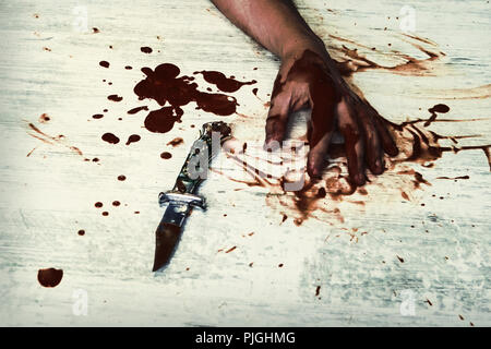 Conceptual image of a victim hand holding a sharp knife with blood on it resting on a white vintage floor. Concept photo of murder and crime Stock Photo