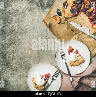 Flat-lay of plum galetta sweet cake in white plates over grey concrete background, top view, copy space. Seasonal Fall or Autumn dessert Stock Photo