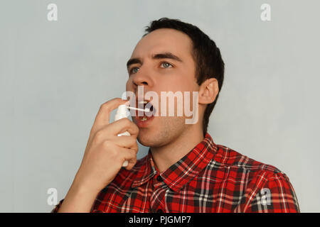 The sick man treats the throat spray medicine spray of white spray. Young guy is sick with a cold. Treatment of swollen glands in the throat. A refres Stock Photo
