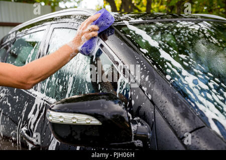 woman washing automobile at manual car washing self service station, cleaning with foam, pressured water. Transportation, auto, vehicle care concept Stock Photo