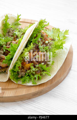 Shrimp tacos on round bamboo board on white wooden table, side view. Mexican cuisine. Stock Photo