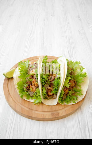 Shrimp tacos on round bamboo board on white wooden table, side view. Mexican cuisine. Copy space. Stock Photo