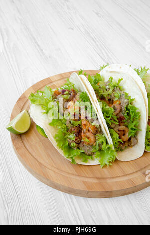 Shrimp tacos on round bamboo board on white wooden table, low angle view. Mexican food. Stock Photo