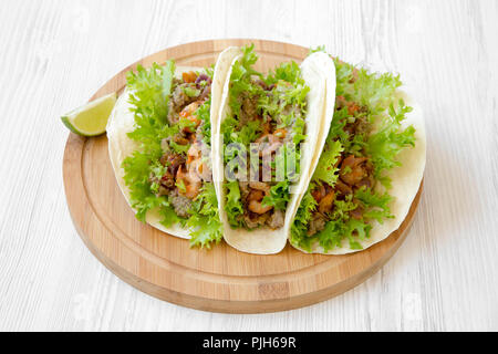 Shrimp tacos on round bamboo board on white wooden surface, low angle view. Mexican food. Stock Photo