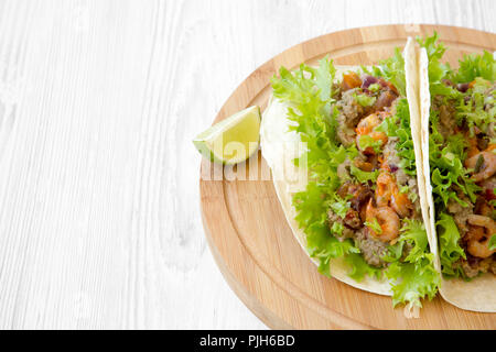 Shrimp tacos on round bamboo board on white wooden background, low angle view. Mexican food. Space for text. Close-up. Stock Photo