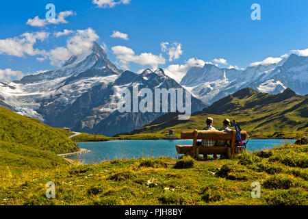Hikers pausing on a wooden bench at lake Bachalpsee, behind the summits Schreckhorn and Finsteraarhorn, Grindelwald Stock Photo