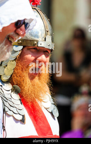 Mature man with orange bushy beard, close up of face from side view, as he speaks. Dressed as medieval knight with armour and helmet on. Stock Photo