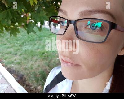a beautiful business Caucasian middle-aged woman with red hair in optical glasses sits on a bench in the Park and takes a selfie on her smartphone. Stock Photo