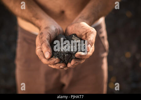 poor middle-aged man holding the hands of stone coal for sale Stock Photo