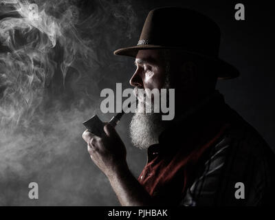 dramatic portrait of senior man in hat smoking tobacco pipe. Profile view of Austrian, Tyrolean, Bavarian old man Stock Photo
