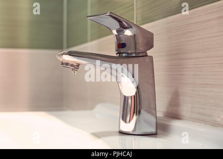 chrome faucet washbasin. Closed the tap dripping water in the bathroom. Waste of water. crane silver color with white sink in the bathroom Stock Photo