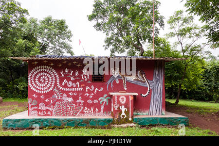 MUMBAI, INDIA – August 9 2018: Colourful mural on a Warli temple, surrounded by trees. Shows traditional scenes of farming, domestic animals, village  Stock Photo