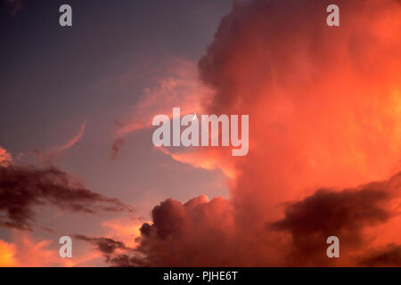 Crescent moon behind intense red, orange and pink clouds Stock Photo