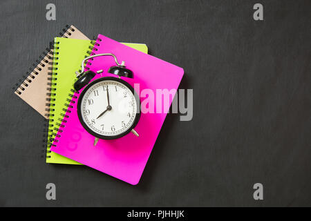 Colorful school supplies and alarm clock on black chalkboard. Top view, flat lay. Stock Photo