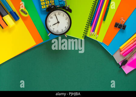 Colorful school supplies, book, and alarm clock on green. Top view, flat lay, copy space. Stock Photo