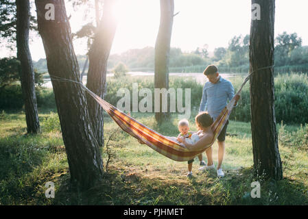 Young sympathetic family - mom, dad and son rest in the nature, sitting in a hammock Stock Photo