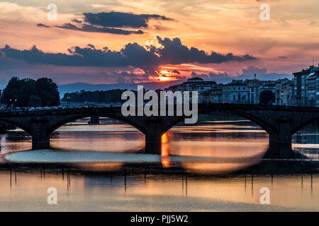 Ponte alla Carraia spans the River Arno in the city of Florence. Here the dramatic sky, reflection and stillness at sunset is captured. Stock Photo