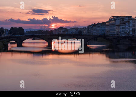 Ponte alla Carraia spans the River Arno in the city of Florence. Here the dramatic sky, reflection and stillness at sunset is captured. Stock Photo