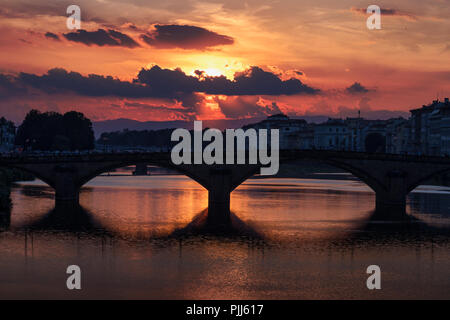 Ponte alla Carraia spans the River Arno in the city of Florence. Here the dramatic sky, reflection and stillness at sunset is captured. Stock Photo